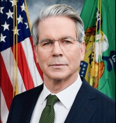 An official portrait of a man in a dark suit standing in front of the American and Department of the Treasury flags.