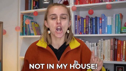 The image features a woman wearing an orange jacket with the phrase "not in my house!" written above her head, as if she's about to make a statement or joke related to the content of the post. The background includes bookshelves filled with various books and decorations, suggesting that this scene takes place in a room where reading and learning are valued.