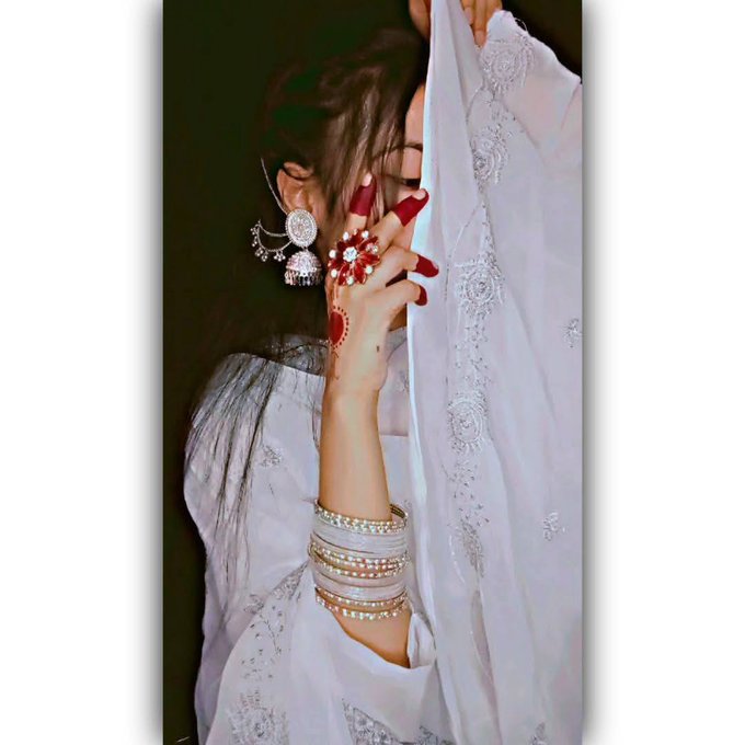 The image features a woman wearing white clothing, including a dress and bangles. She has her hand partially covered by a white cloth or scarf while looking at the camera. The background of the photo appears to be black, which contrasts with the white elements in the foreground. There is also text present in the image that reads "Happy Monday gTria Hope you get start exploring @useTria both app and @MindoAI stay conected with @wallchain and @Polymarket".