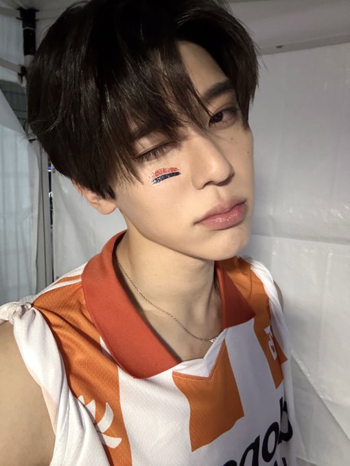 A young man with dark hair wearing an orange and white Dongguk University jersey, with face paint reading 'EVER' on his cheek.