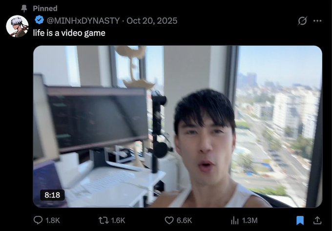 A screenshot of a pinned tweet by @MINHxDYNASTY posted October 20, 2025 with the caption "life is a video game," showing a man in a white tank top on video (timestamp 8:18) in a high-rise room with a city view, which has gained 6.6K likes and 1.3M views, likely referencing his experience using AI to navigate a trading or investment "video game" challenge.