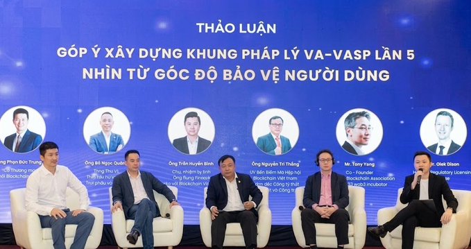A panel discussion at a conference with five men seated on white chairs, beneath a blue screen with Vietnamese text discussing legal frameworks for virtual assets and user protection, featuring speaker names like 'Phan Đức Trung' and 'Tony Vũng'.