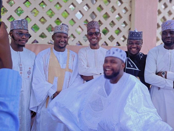 A group of six men in traditional attire pose together smiling, with one seated man in the center surrounded by others wearing caps and flowing robes. The image ties to the post's challenge of memorizing a long Solana token contract address, humorously suggesting that retaining the complex alphanumeric string "2vvw3cSwibzGD6SgW9QzRaBdmjkYrvs218DUy6VWpump" would require a memory as sharp as a gathered assembly of focused minds.