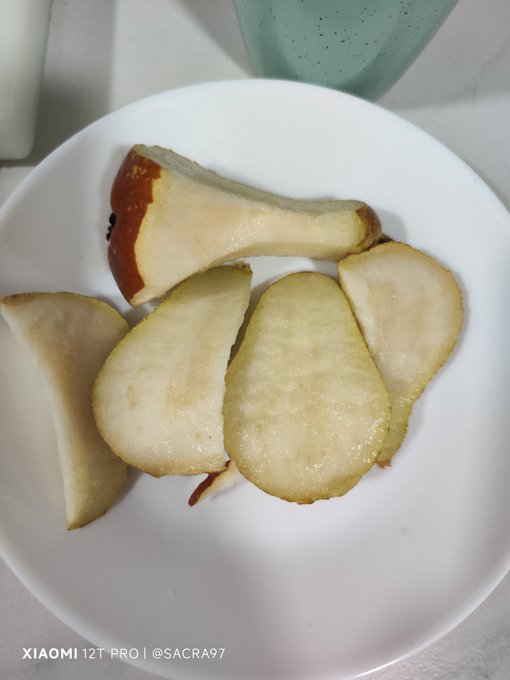 The image features a white plate with several pieces of fruit, including pears and apples, arranged on top of it. The background appears to be a kitchen counter or dining table, suggesting that this scene takes place during mealtime. The photo is tagged with an interesting caption that reads "#hive desde cualquier rincón del mundo". This caption likely refers to the idea that food brings people together and can be enjoyed in various settings, regardless of cultural differences.