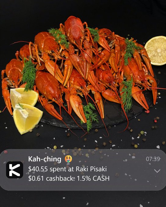 A close-up of a heap of cooked crayfish on a slate platter, garnished with lemon wedges, dill, and scattered peppercorns, overlaid with a notification showing "Kah-ching: $40.55 spent at Raki Pisaki, $0.61 cashback: 1.5% CASH" to illustrate a quick cashback confirmation via @KASTxyz on Solana.