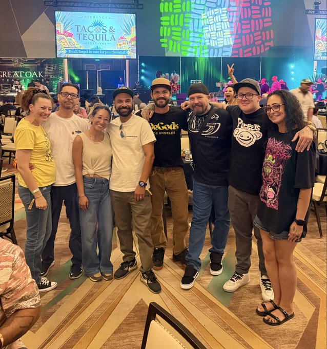 A group of eight friends pose together at the 'Fernandos Taco & Tequila' restaurant (with a banner reading 'Don't forget to vote for your favorite!'), at what appears to be a 'MIAMI' branded event with colorful stage displays in the background.