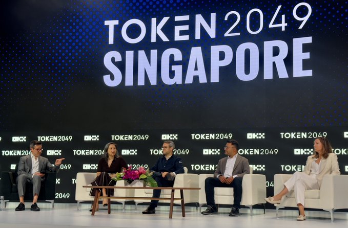 A panel discussion at TOKEN2049 Singapore featuring five speakers seated on a stage with 'OKX' and 'TOKEN2049' branding on the backdrop.