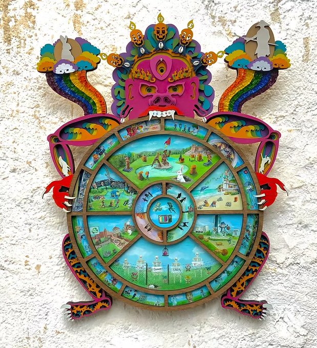 A colorful, ornate Tibetan-style Bhavachakra (Wheel of Life) wall hanging featuring a wrathful deity at the top and intricate scenes depicting various realms and karmic cycles within the wheel.