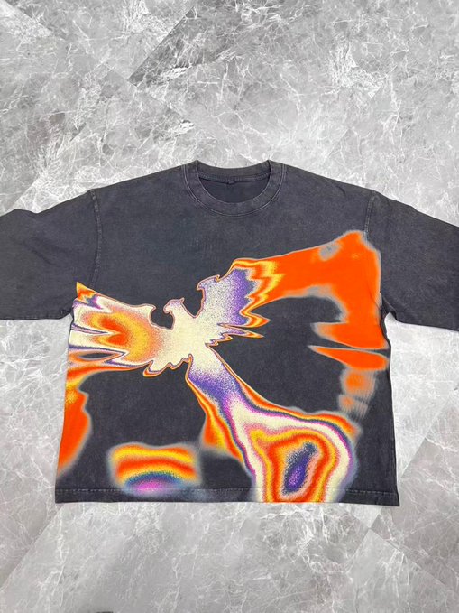 A dark, washed grey t-shirt featuring a vibrant, psychedelic print in orange, purple, and yellow tones resembling a stylized bird or eagle in flight.