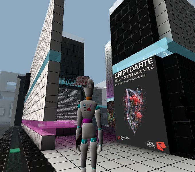 A 3D virtual environment featuring an avatar standing in a city plaza with posters for 'CRIPTOARTE: TERRITORIOS LATENTES' and 'I LOVE THIS PLACE'.