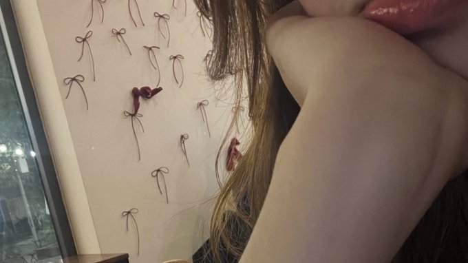 The image features a close-up of a person's face, with their chin resting against a wall adorned with numerous small red bows. The bow arrangement spans across the entire background of the photo, creating an interesting visual effect that draws attention to the subject. The person's chin is visible in the foreground, while the bows are positioned behind them, adding depth and dimension to the image.