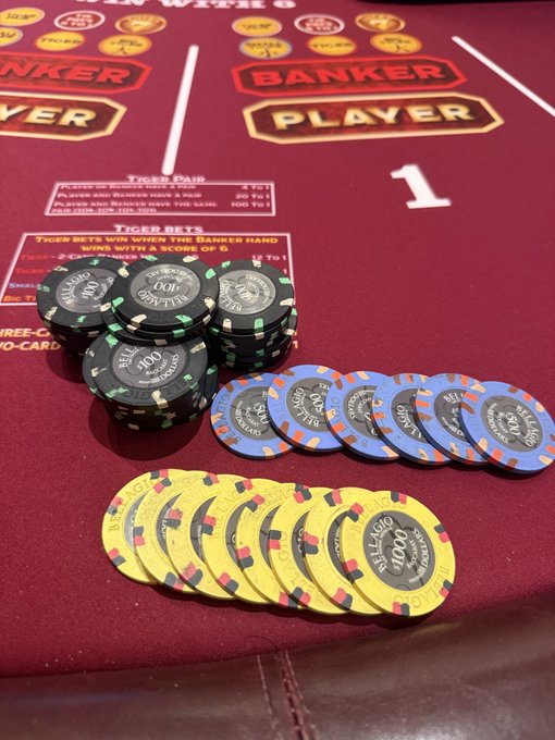 A pile of $100 casino chips—black, blue, and yellow Bellagio chips—resting on a red felt baccarat table marked with "PLAYER," "BANKER," and "TIGER BETS," illustrating the high-stakes private lounge game ranging from $7,000 to $14,000.
