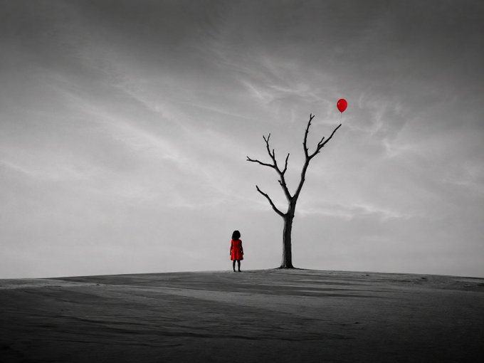 A black-and-white artistic scene of a small girl in a red dress standing before a bare tree, with a single red balloon floating away.