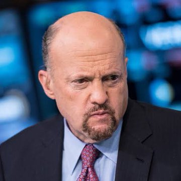 A close-up photo of a bald man with a goatee wearing a dark suit, blue shirt, and pink patterned tie, appearing on a TV news set with a blue background.
