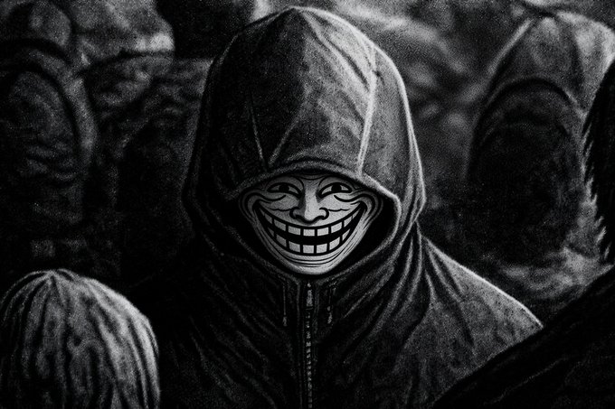 A black-and-white image shows a figure in a dark hooded jacket wearing a wide, grinning Trollface mask, surrounded by other shadowy hooded figures in the background. The menacing, anonymous appearance of the masked figure visually reinforces the post's message that a troll, like $TROLL, may face resistance but cannot ultimately be silenced.