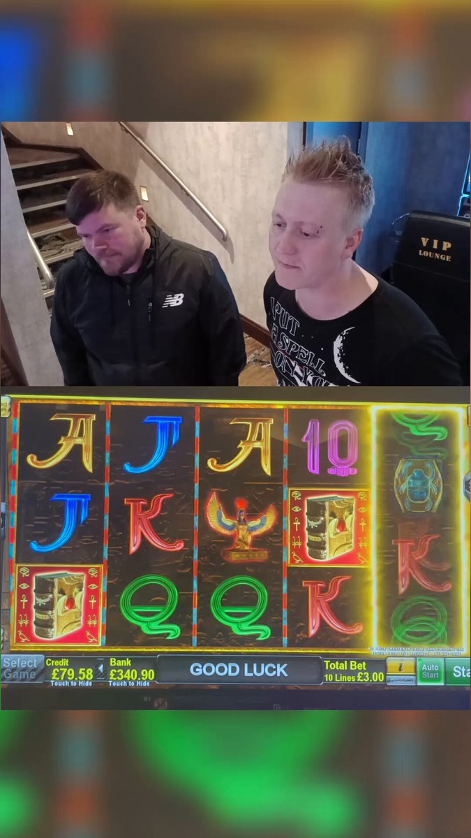 The image shows a slot machine with two men standing next to it, one of whom appears to be taking a photo or recording a video of their gameplay experience. The other man seems to be watching them. There are also some numbers visible on the screen of the slot machine, which could potentially be related to the game's scoring system or other relevant information.