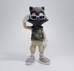 A stylized figurine of an anthropomorphic black cat wearing white-rimmed sunglasses, a floral shirt, and beige pants, posing with one hand adjusting its glasses.