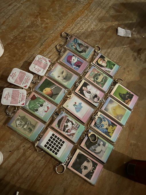 A collection of vintage-looking keychains featuring various photos, stickers, and designs laid out on a wooden floor.