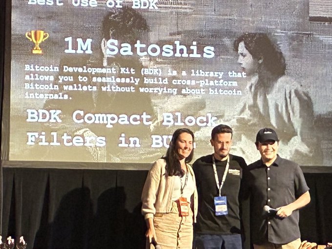 Three people pose in front of a projection screen announcing a "1M Satoshis" prize for "Best use of BDK," with text highlighting "BDK Compact Block Filters in BULL" — an award the caption credits to BULL developer Azad for winning at the BTC++ Toronto hackathon with an overnight proof-of-concept integrating compact block filters into the BULL wallet for more private Bitcoin syncing.