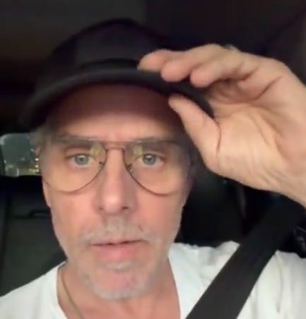 The image shows Hunter Biden tipping his black cap while seated in a car, wearing tinted glasses and a white shirt. The selfie appears to be a still from the X video where he discusses his "$LAPTOP" memecoin's dramatic price surge and market cap.