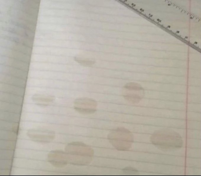 A lined notebook page with several circular grease or oil stains and a metal ruler visible at the top right corner.