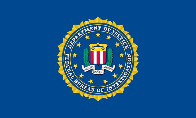 The image shows the seal of the Federal Bureau of Investigation (FBI), part of the U.S. Department of Justice, set against a solid blue background. It directly relates to the news, as the FBI has reportedly arrested a suspect accused of distributing malware through Steam games to steal over $220,000 in cryptocurrency from victims.