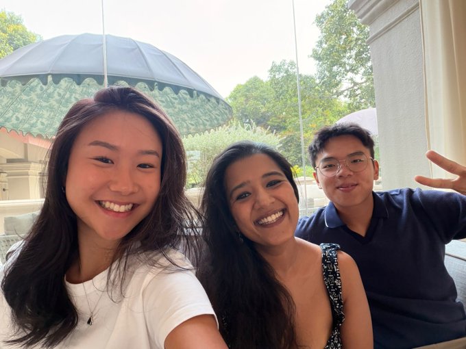 The Bitget comms team smiles for a selfie at Token2049, posed together in front of a decorative parasol and lush greenery as they arrive at the conference.