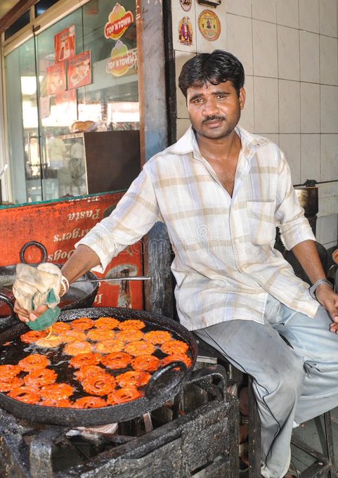 A street vendor in India sits behind a large black pan, frying orange-colored jalebi sweets while holding a green squeeze bottle. Signs reading "Coca-Cola" and "Thumbs Up" are visible in the background, along with a partial view of bread or pastries on display.

The image humorously contrasts the post's reference to "Frank DeGods" lacking insider crypto knowledge by showing a humble street food vendor engaged in traditional, straightforward work—juxtaposing the speculative, info-driven world of meme coins with honest, hands-on labor.