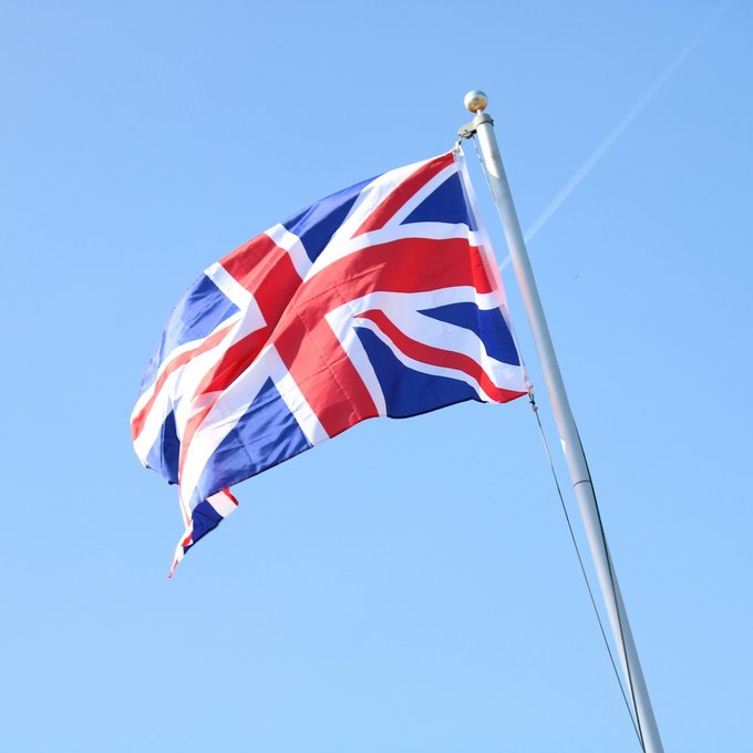 A vibrant Union Jack flag billows against a clear blue sky, symbolizing the United Kingdom as it prepares to grant the Bank of England a new mandate supporting innovation in digital payments, including stablecoins.