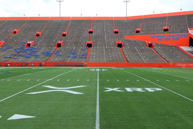 An empty football stadium shows a green field marked with XRP logos, with 'NATIONAL CHAMPIONS' banners visible in the orange stands.