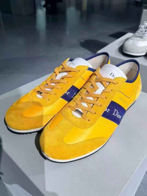 Yellow Dior sneakers with blue 'Christian Dior' branding displayed on a gray surface.
