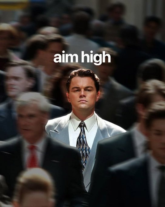 Leonardo DiCaprio in a gray suit stands out among a crowd of people, with the text 'aim high' displayed above him, referencing The Wolf of Wall Street.