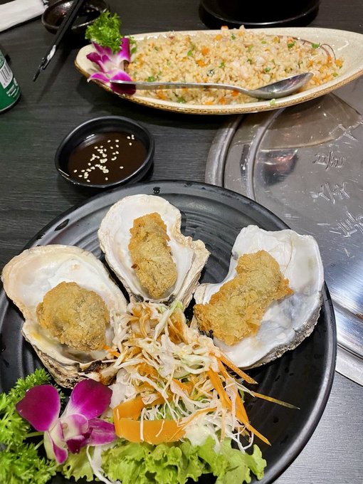A plate of fried oysters on the half shell served with shredded vegetables and a side of fried rice, with a small dish of dipping sauce.