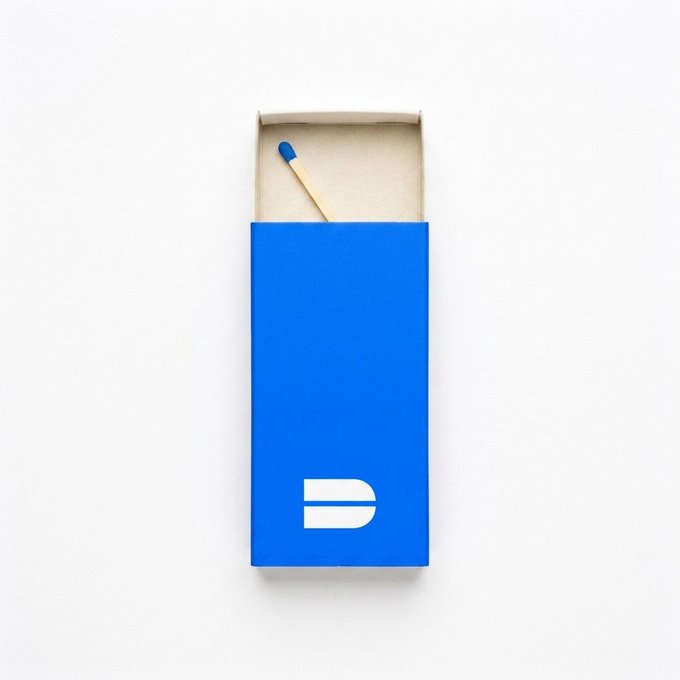 A minimalist product photo of a single wooden matchstick inside a blue matchbox with a white pill-shaped logo on a plain white background.