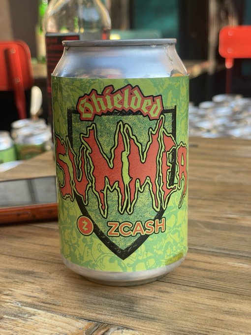 The image features a can of beer with a green shield design that reads "Summer", indicating that the beer is made during the summer season. The can also has an orange label, which adds a pop of color to the scene. There are other cans in the background and on the table as well, suggesting that this might be a gathering or event where people have brought their own beverages. A cell phone is placed near one of these cans, possibly used for capturing memories or communicating with friends during the summertime celebration.

The image also contains text that reads "Splash into summer fun, bottoms up!", which could be an inside joke among friends or a playful way to describe enjoying summer activities while drinking beer.