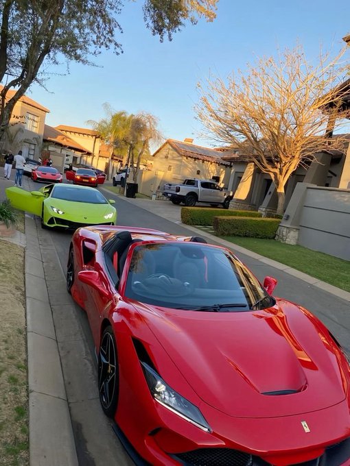 A photo of a red Ferrari sports car parked on a residential street, with a green Lamborghini and other vehicles visible in the background.