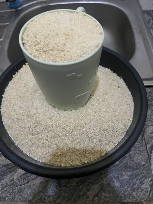 A light green ceramic mug filled with white powder (likely ground rice or similar) sitting on a matching base within a black tray, placed near a kitchen sink.