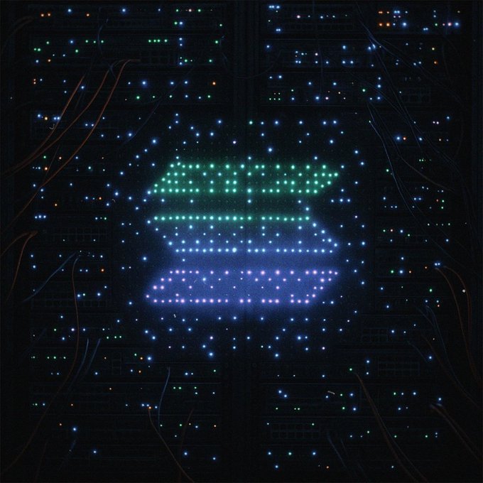 An artistic image showing a glowing green and purple Bitcoin logo formed by lights on the surface of a dark computer motherboard or circuit board.