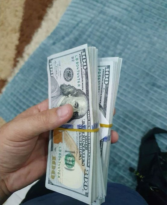 A hand holds a thick stack of $100 bills bound with rubber bands, displayed against a blue textured background—visually reinforcing the post's aspirational "Let's get rich together" message through imagery of substantial cash wealth.