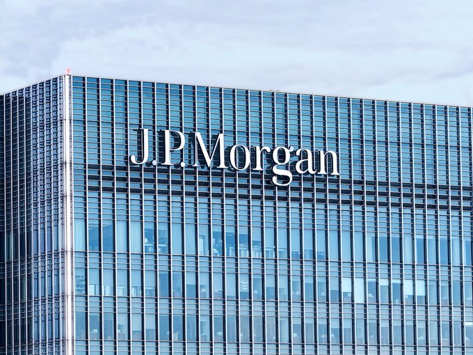 The iconic "J.P. Morgan" sign is displayed on the side of a modern glass building, representing the institution quoted in the post about Bitcoin's structural risks.