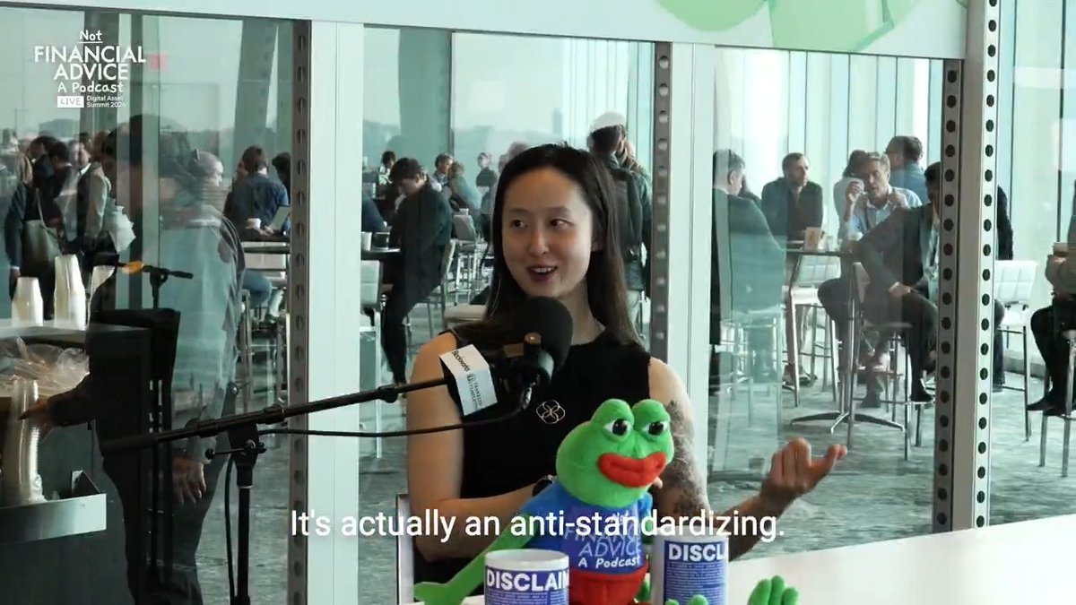 A woman speaks into a microphone on the 'Not Financial Advice' podcast (Live Digital 2025), saying 'It's actually an anti-standardizing,' while holding a Pepe frog plushie beside a 'DISCLAIMER' mug.