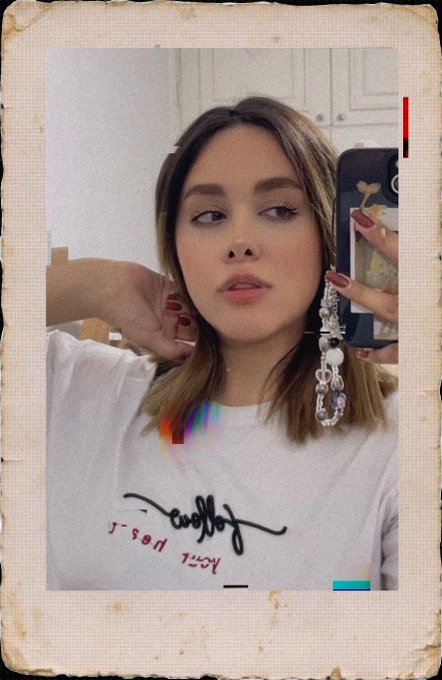 A polaroid-style photo of a woman taking a mirror selfie, wearing a white t-shirt and holding a phone, with the name 'Bettie' and 'just' 'you!' written in script on the photo.