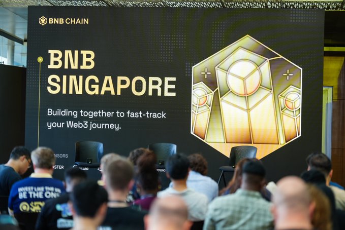 The image shows a large digital banner at the BNB Singapore event displaying "BNB CHAIN," "BNB SINGAPORE," and the tagline "Building together to fast-track your Web3 journey," with an audience gathered in front. The scene captures attendees facing the stage, fitting the post's announcement about BNB Singapore landing on 7 October and inviting people to attend.