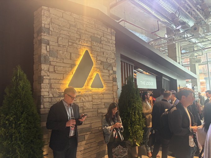 Attendees at a Binance-hosted networking area called 'THE LODGE', with a large illuminated Binance logo mounted on a stone wall.