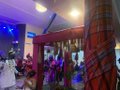 A small, blurry image showing what appears to be an interior scene with people gathered near windows and green plants, possibly a shop or gallery setting.