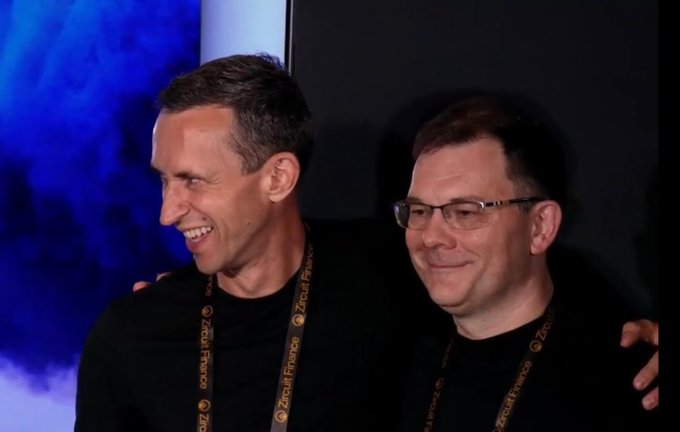 The image features two men standing next to each other, both wearing black shirts with gold necklaces around their necks. They are smiling at the camera, suggesting a sense of camaraderie or shared accomplishment. The background appears to be a dark room, which contrasts with the bright blue color in the top left corner and adds depth to the image. The post includes text that reads "What an amazing start for Claims! Winning the pitch competition in the Louvre with such great judges, competitors, and so much support from the audience was a big honor".