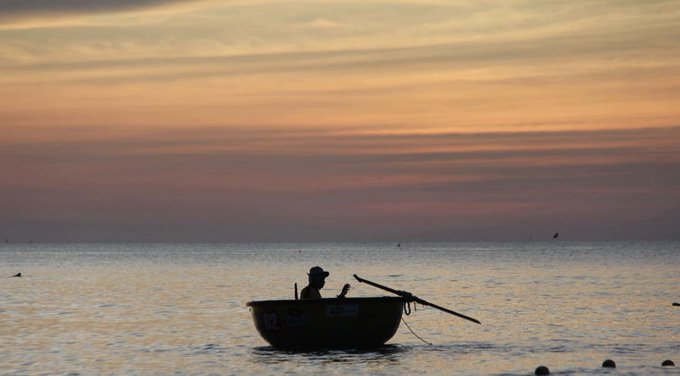 A lone fisherman in a small round basket boat sits silhouetted against a golden sunset over calm waters, with the number "02" visible on the side of the vessel, evoking the patient "rise and grind" spirit of the post.