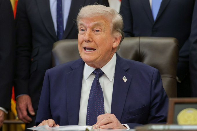 The image shows President Donald Trump sitting at a desk, surrounded by people who appear to be his advisors or staff members. The man is wearing a suit and tie, indicating that he is in a formal setting. The scene takes place during a meeting where Trump is discussing various topics with his team. One of the topics being discussed is Iran, which has led to a significant drop in stock markets worldwide. This event highlights the unpredictability and potential impact of President Trump's statements on financial markets.