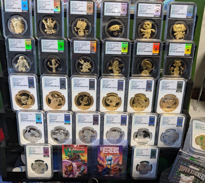 A display case showcases numerous graded Pokémon TCG coins, including various Pikachu, Eevee, and other Pokémon designs, alongside what appear to be Pokémon cards labeled 'VeeFriends' and 'SUPER STICKERS.'