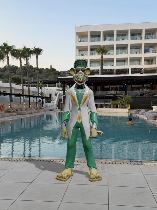 A person in a green and white costume with a menacing, sharp-toothed animal mask stands by a swimming pool at a resort, with a multi-story hotel building behind them.